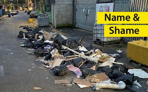 Image of a fly tip with bags of rubbish, pieces of wood all along the side of a road